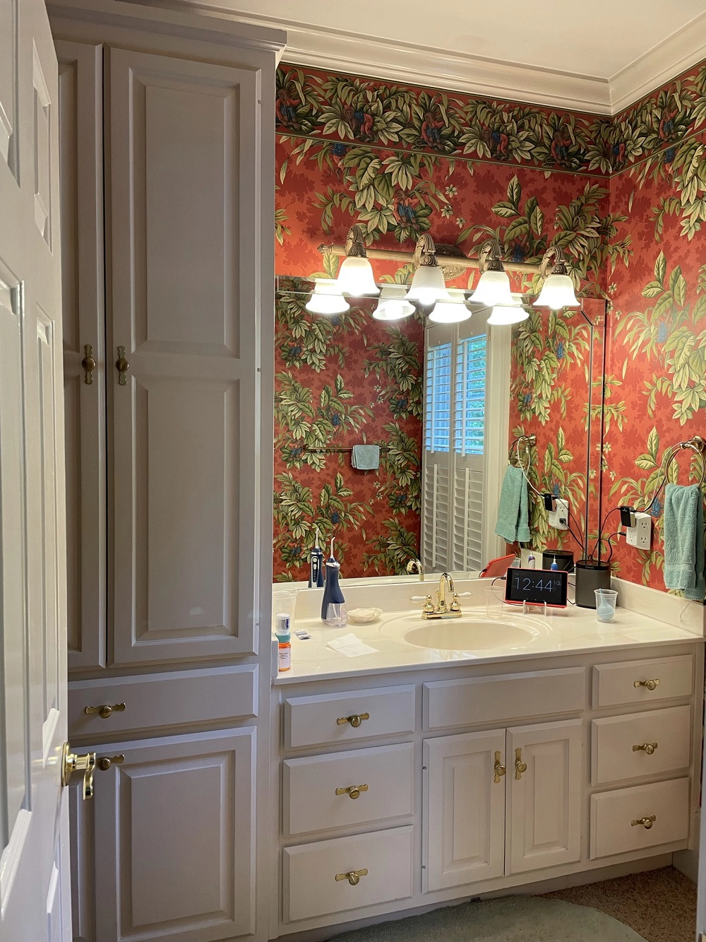 A dark and dated 1990s bathroom design with red wallpaper and white cabinets.