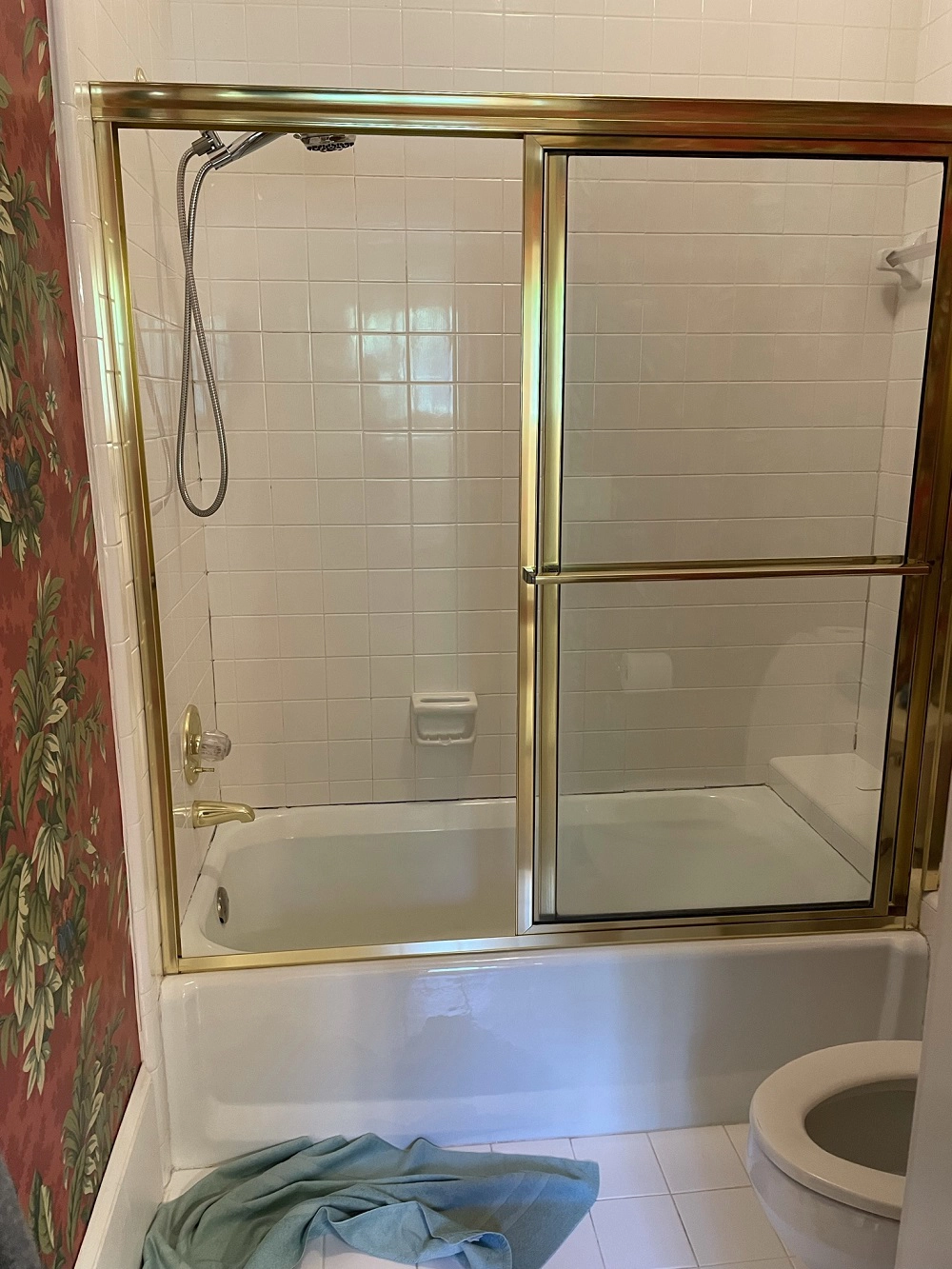 A 1990s bathroom with bright brass tub enclosure, dark wallpaper, and white floor and shower tiles